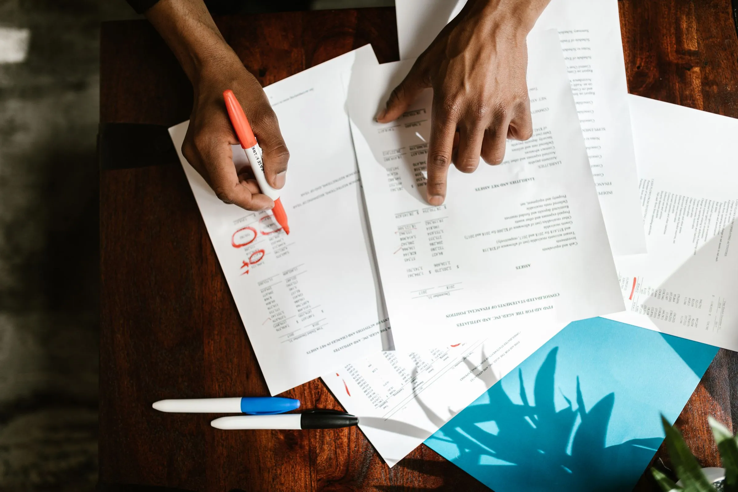 Hands reviewing and annotating printed documents with a marker