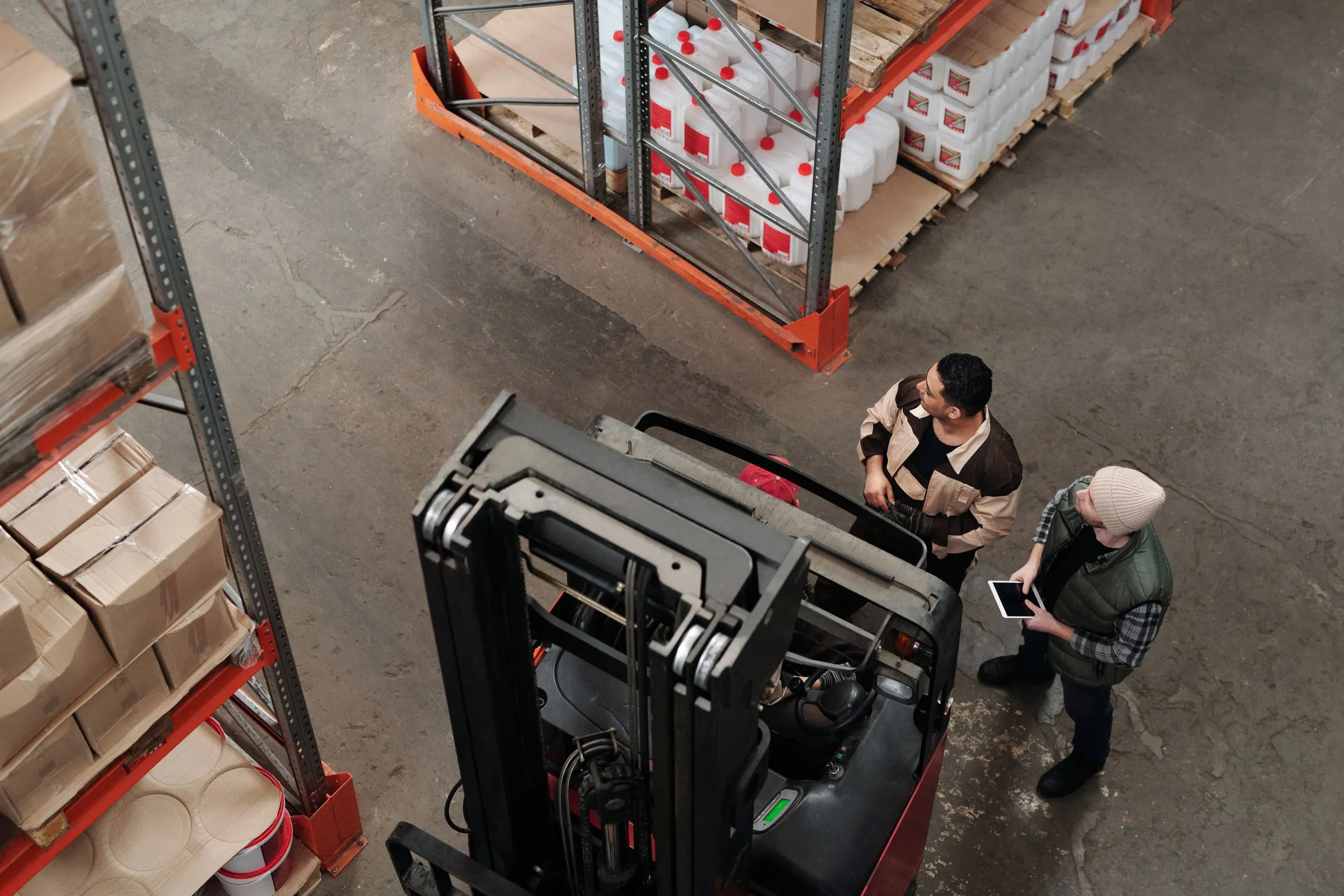 Two warehouse workers beside a forklift, one holding a tablet