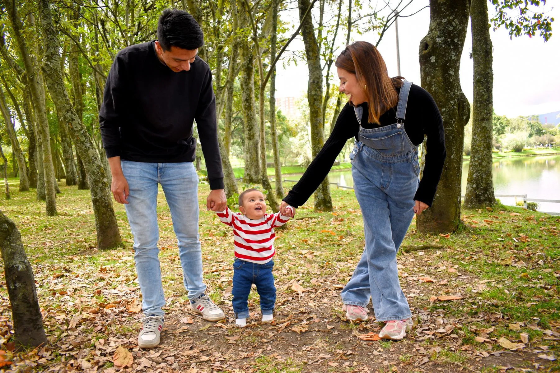 Two parents holding a toddler's hands while walking in a park