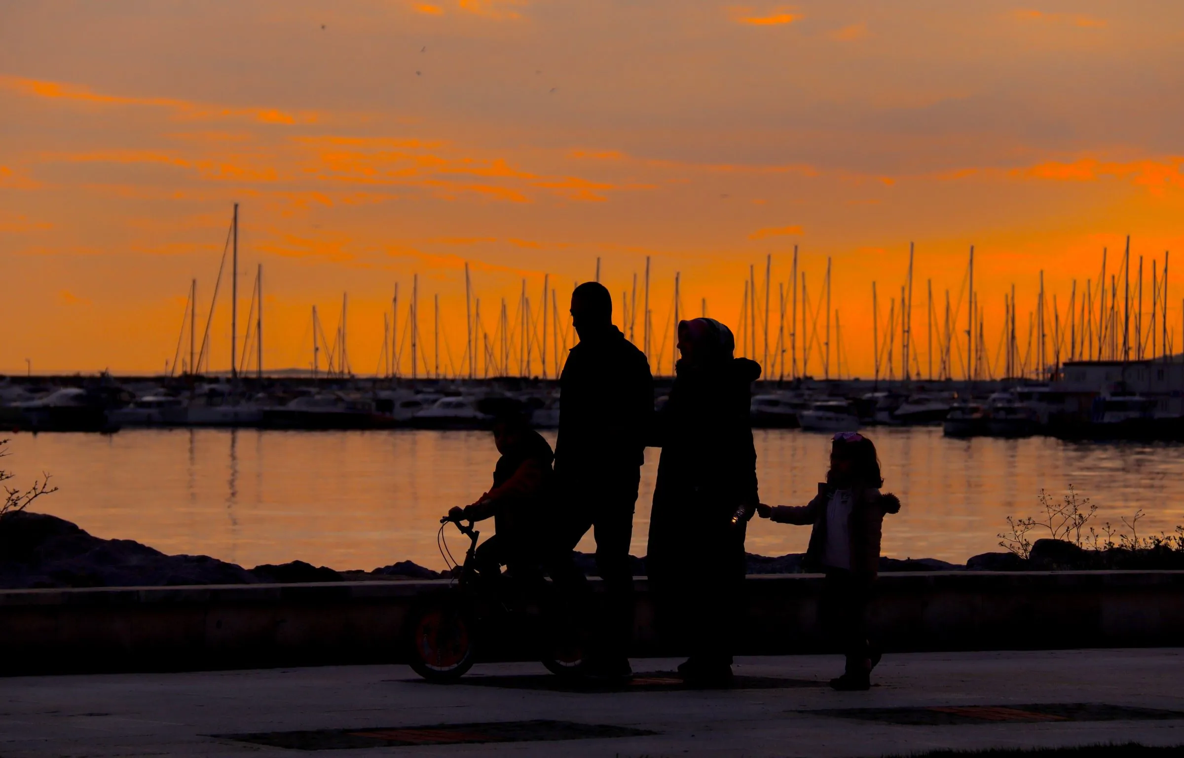 A family with two children silhouetted against a sunset at a harbour