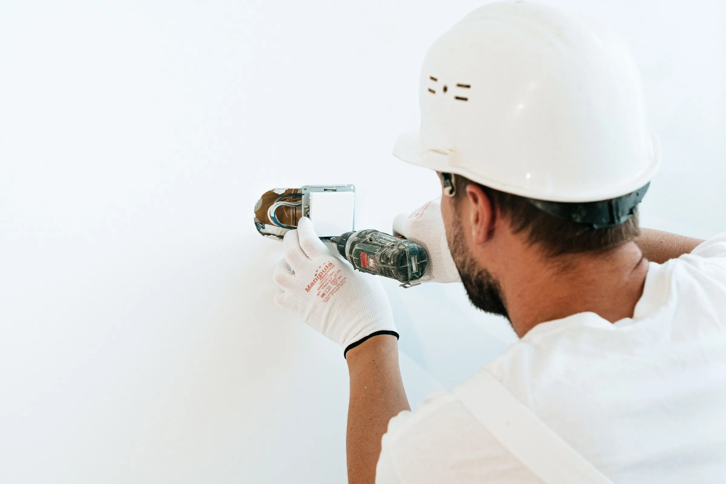 A tradesperson in a hard hat fitting an electrical outlet