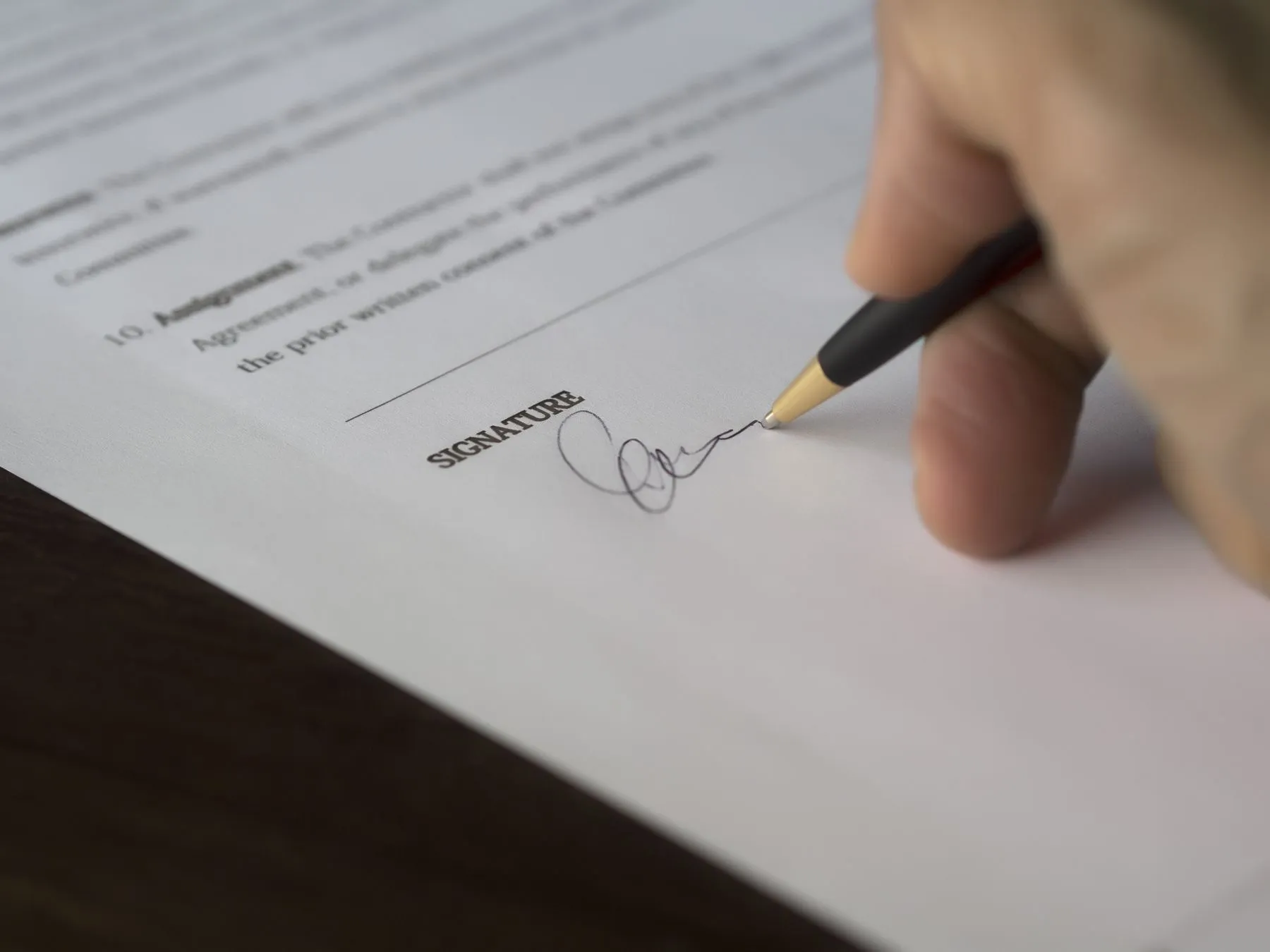 A hand signing an agreement on the signature line
